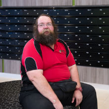 A man sits on a plush chair in front of a wall of letter boxes.