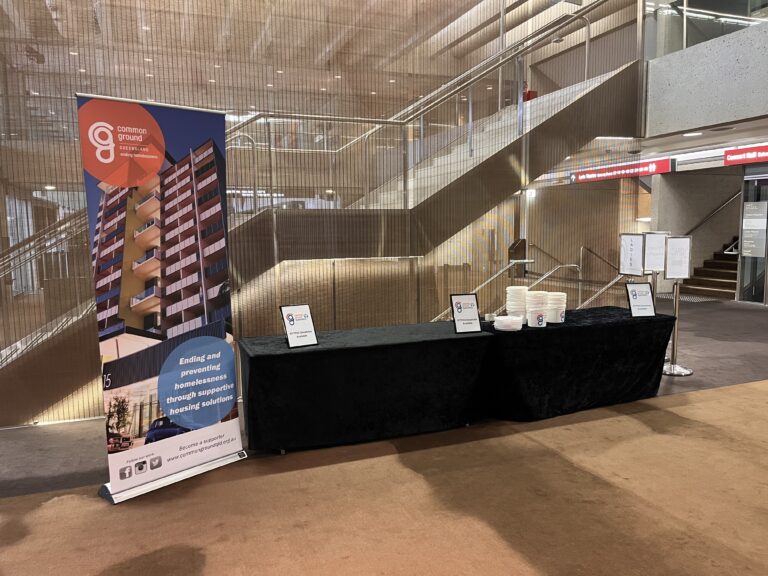 An image of a stall with the Common Ground Queensland banner and a black satin table.